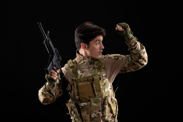 Front view military serviceman in uniform aiming his rifle on black floor