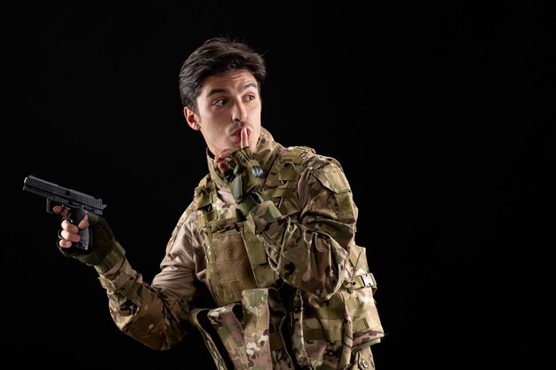 Free photo front view military serviceman in uniform holding gun on black wall