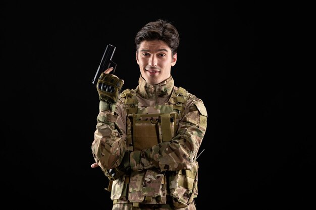 Front view of military serviceman in uniform holding gun black wall