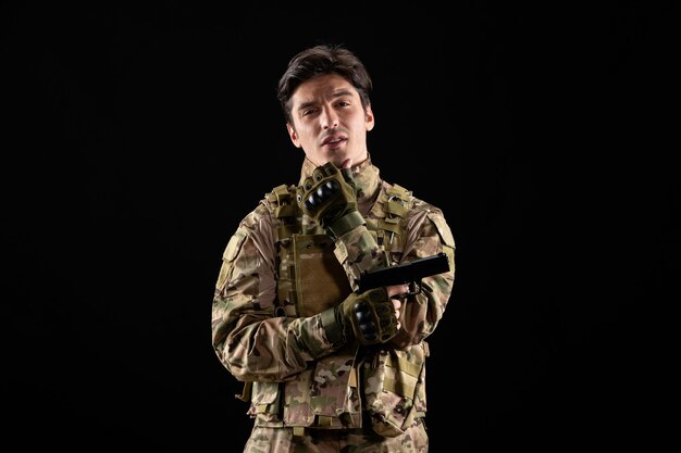 Front view of military serviceman in uniform holding gun on black wall