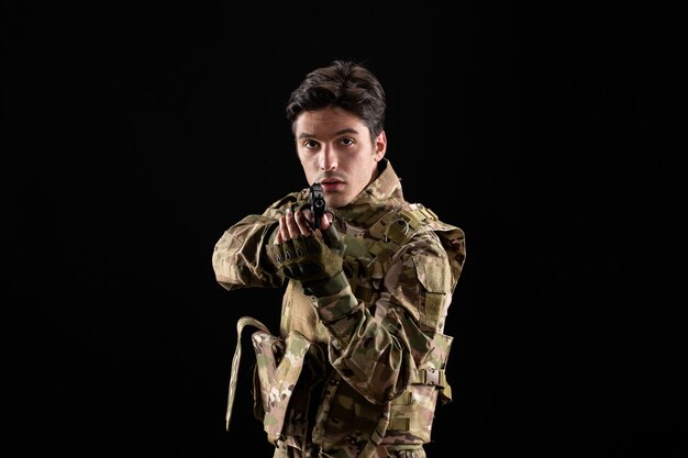 Front view of military serviceman in uniform with gun on black wall