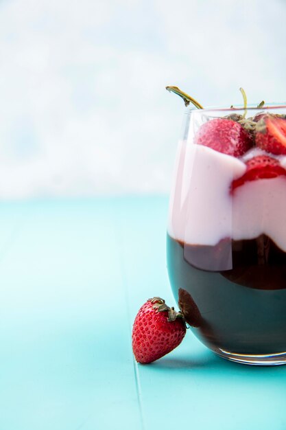 Front view of milkshake with chocolate and strawberries on a glass on a blue table on a white surface