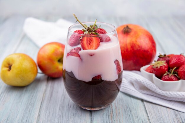 Front view of milkshake with strawberry and chocolate with apples and pomegranate on grey surface