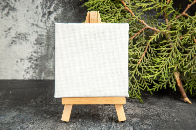 Front view mini canvas on wooden easel pine branch on grey background