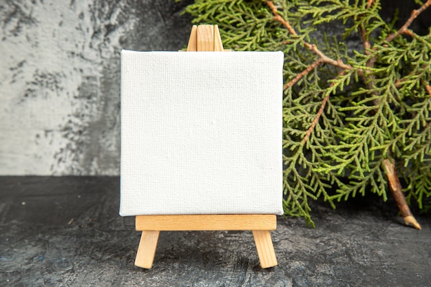 Front view mini canvas on wooden easel pine branch on grey