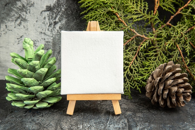 Free photo front view mini canvas on wooden easel pine branch pinecones on grey