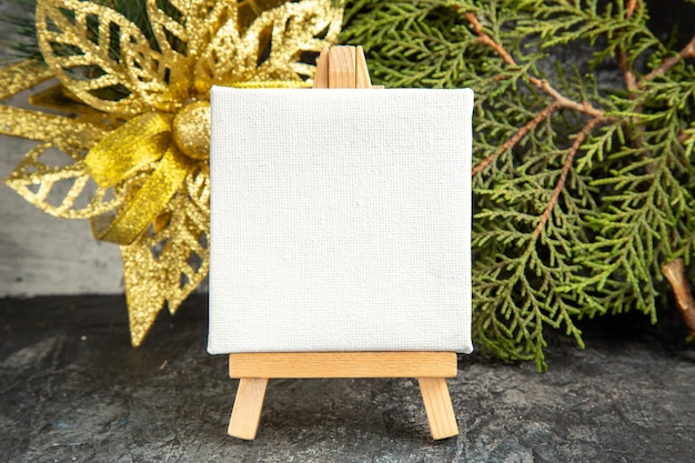 Front view mini canvas on wooden easel pine branch xmas ornament on grey background