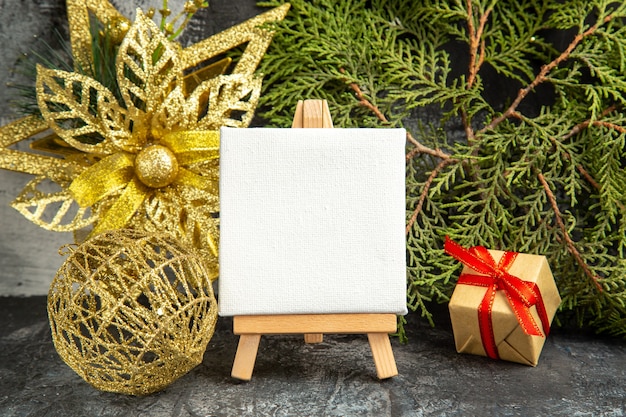 Front view mini canvas on wooden easel pine branch xmas ornaments on grey background