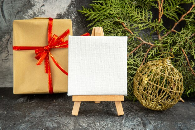 Front view mini canvas on wooden easel pine branch xmas ornaments mini gift on grey background
