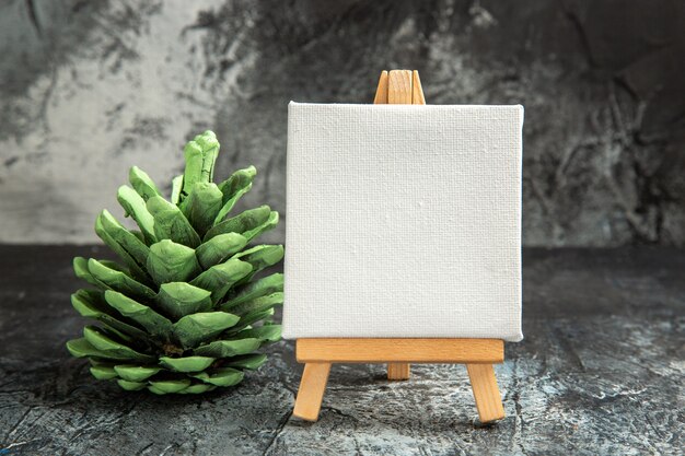 Front view mini white canvas with wooden easel green pinecone on dark isolated background