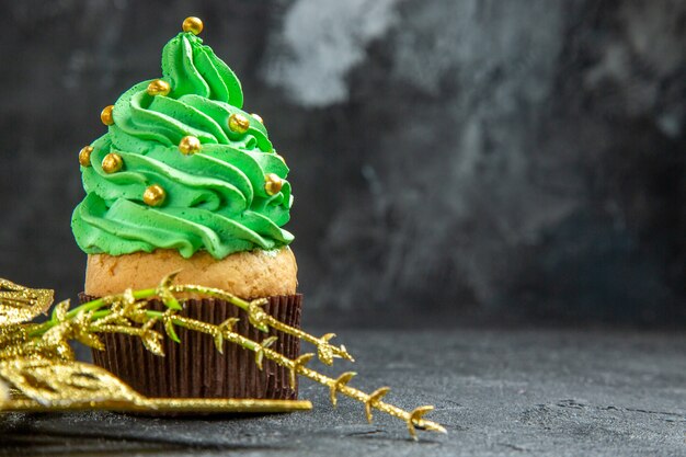 Front view mini xmas tree cupcake and golden hanging ornament on dark background