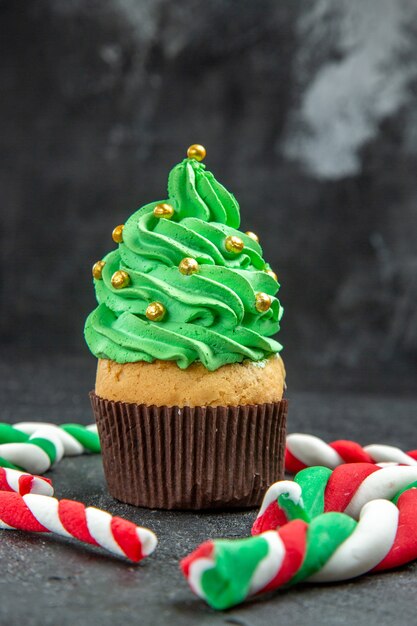 暗い背景の正面図のミニクリスマスツリーカップケーキとクリスマスキャンディー