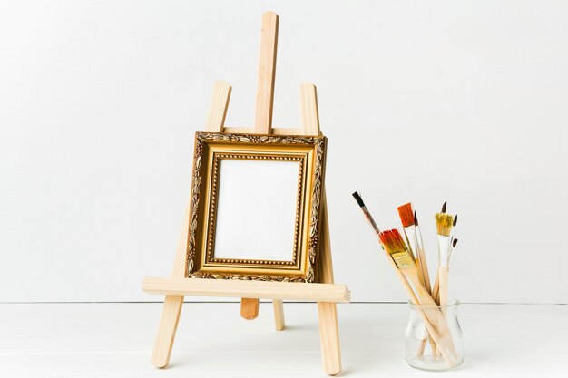 Front view minimalist frame on easel and brushes