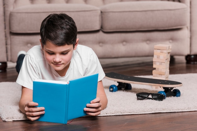 Front view of modern boy sitting on floor with book