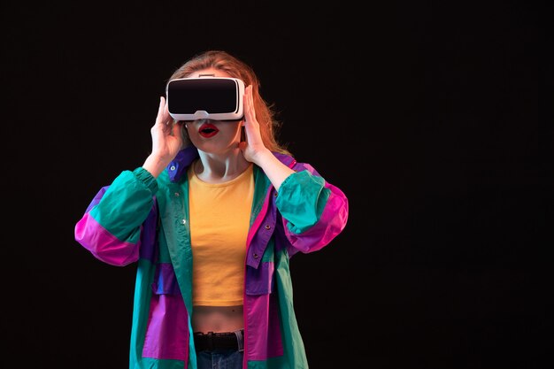 A front view modern young lady in colorful coat orange t-shirt playing virtual reality on the black background gaming interactive play