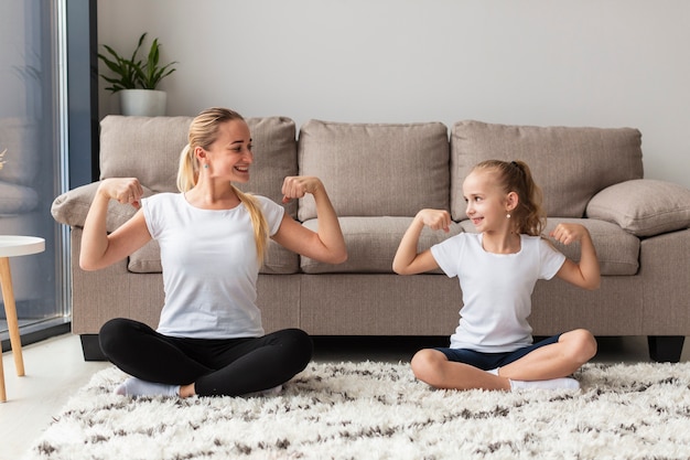 Free photo front view of mother and daughter at home showing off biceps