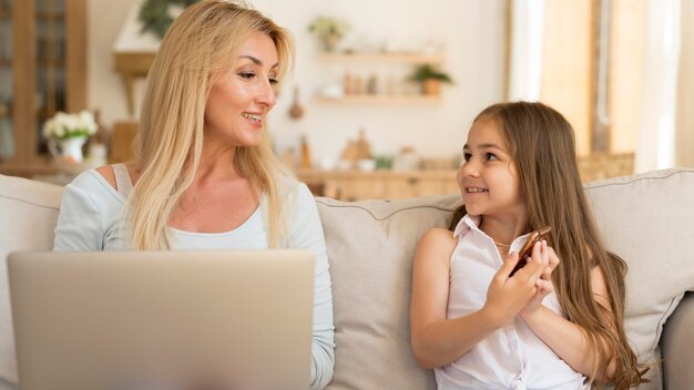 Front view of mother and daughter at home with laptop and smartphone