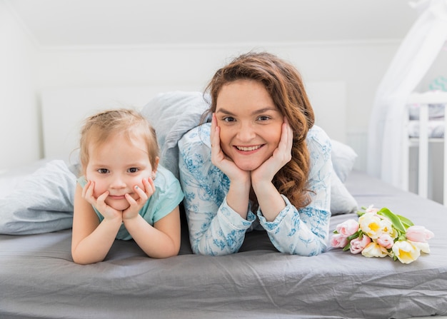 Front view of mother and daughter looking at camera while lying on bed at home