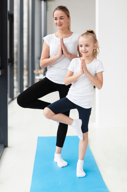 Front view of mother and daughter practicing yoga pose at home