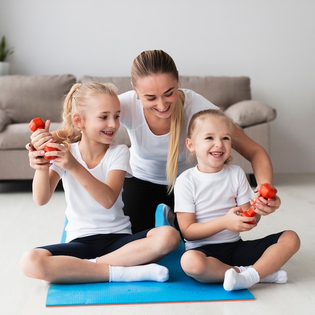 Front view of mother posing with daughters at home while holding weights