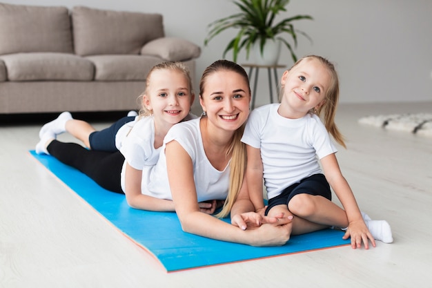 Front view of mother posing with daughters on yoga mat at home