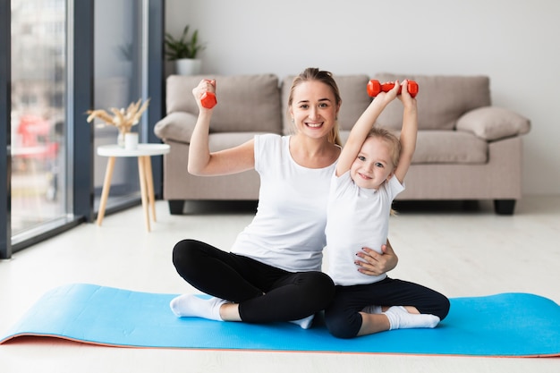 Front view of mother with daughter posing while holding weights