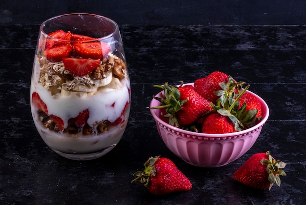 front view muesli with fruits and nuts in a glass with a pink bowl with strawberries
