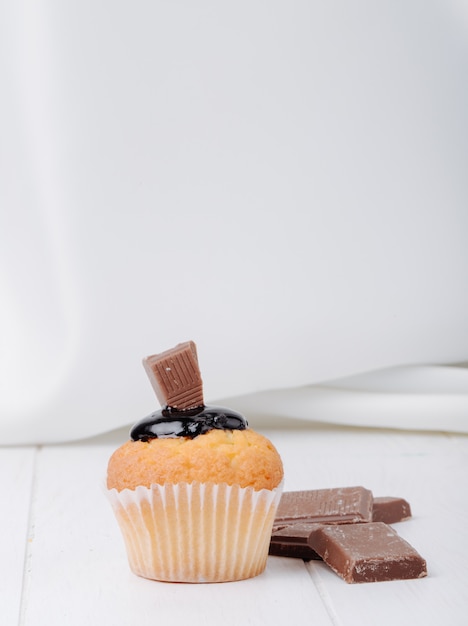 Muffin di vista frontale con glassa al cioccolato e cioccolato su una superficie bianca