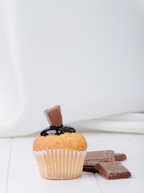 Маффин спереди с шоколадной глазурью и шоколадом на белой поверхности