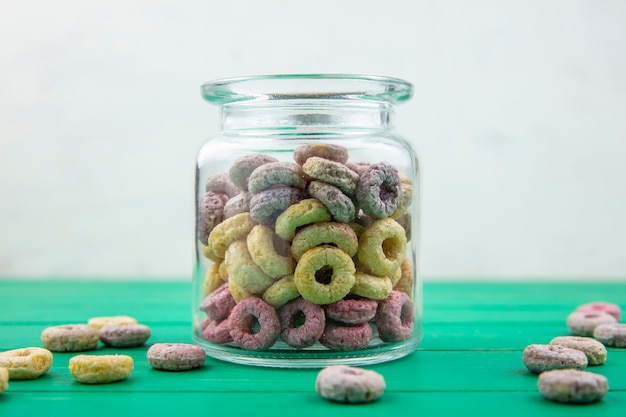 Free photo front view of multicolored cereals on a glass jar with cereals isolated on green table on white surface