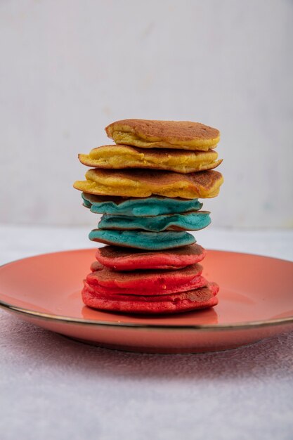 Front view multicolored pancakes on an orange plate  on a white background