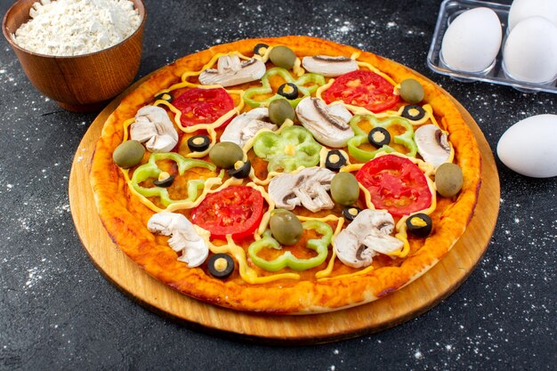 Front view mushroom pizza with red tomatoes bell-peppers olives and mushrooms all sliced inside with eggs and flour on grey