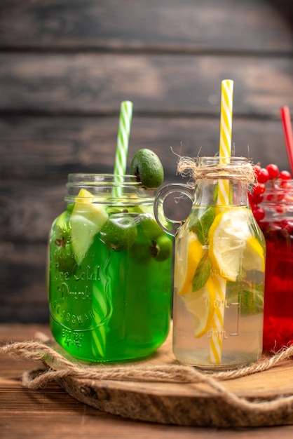 Front view of natural organic fuit juices in bottles served with tubes on a wooden cutting board