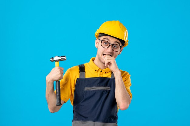 Front view of nervous male builder in uniform with hammer on blue 