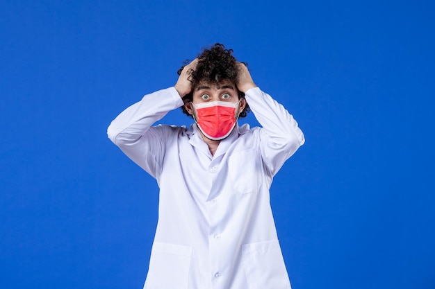 Front view nervous male doctor in medical suit with red mask on blue background drug virus covid- vaccine health medicine hospital pandemic colours