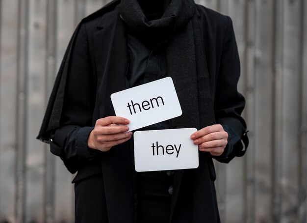 Front view non binary person holding pronouns cards