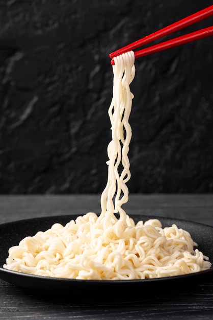 Front view noodles in chopsticks over plate