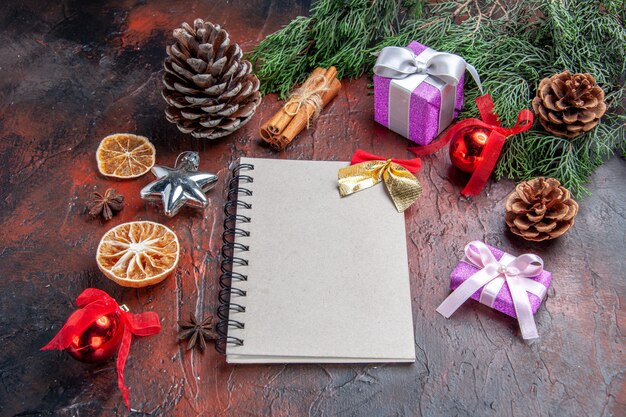 正面図小さな弓松の木の枝の円錐形のクリスマスツリーのおもちゃとギフトシナモンスターアニスと濃い赤の背景のノートブック