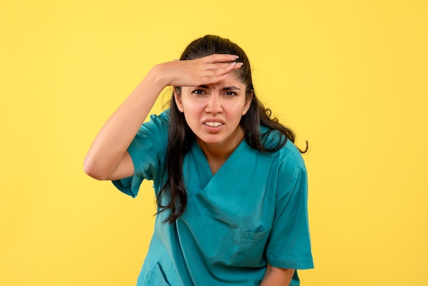 黄色の背景に立っている制服を着た女性医師を観察する正面図