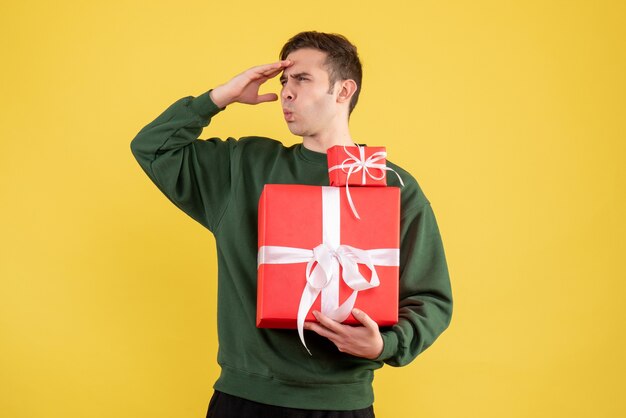 Front view observing young man with xmas gift standing on yellow background