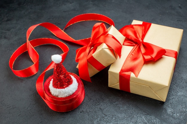 Бесплатное фото Вид спереди красивых подарков с красной лентой и шляпой санта-клауса на темном столе