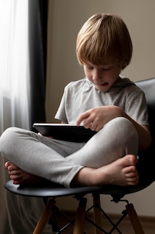 Вид спереди мальчика, сидящего в чарте и использующего планшет