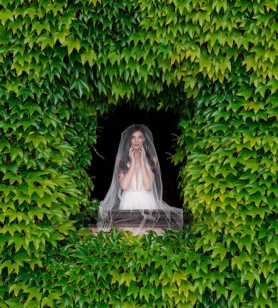 Вид спереди невесты, стоящей перед окном с рамкой из свежей зелени