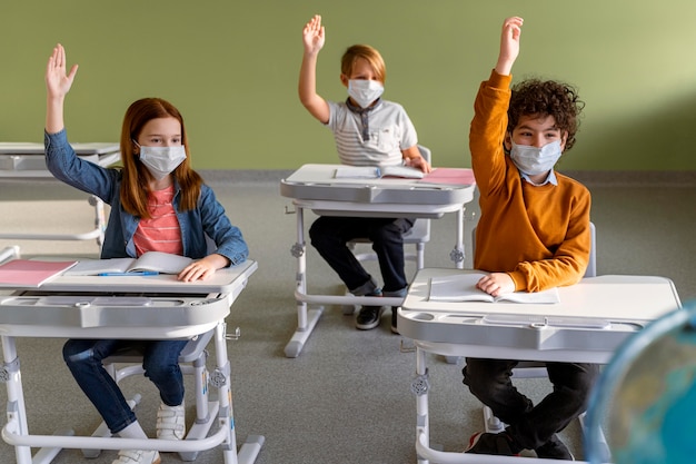 Бесплатное фото Вид спереди детей с медицинскими масками в школе, поднимая руки