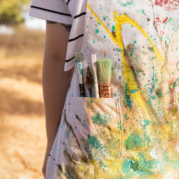 무료 사진 페인트와 붓으로 가득한 앞치마가있는 여성 예술가의 전면보기