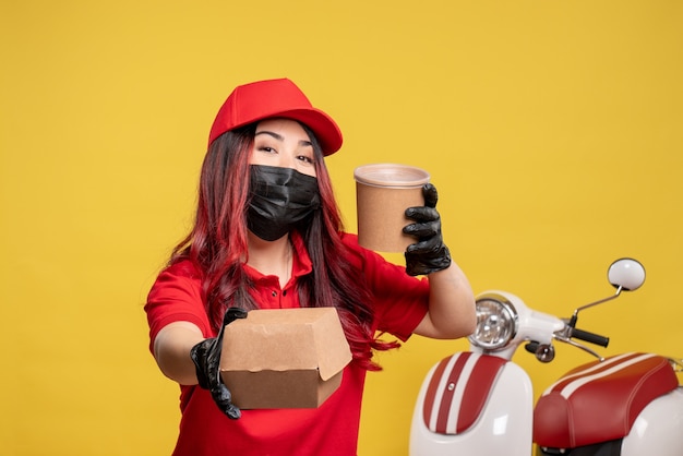 Бесплатное фото Вид спереди курьера-женщины в маске с доставкой еды на желтой стене