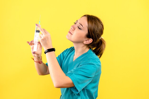 Вид спереди ветеринара-женщины, держащего инъекцию на желтой стене Бесплатные Фотографии