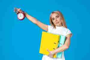 Бесплатное фото Вид спереди работницы, держащей папку и часы на синей стене