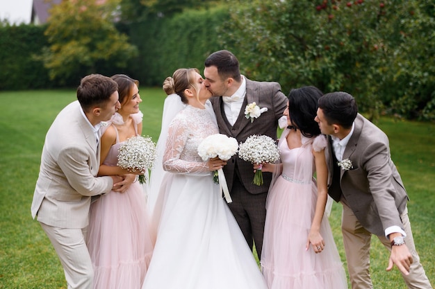 무료 사진 축제 의상을 입은 친구들의 앞모습은 양쪽에 서서 결혼식을 하는 동안 행복하고 키스하는 신혼부부를 바라보는 것입니다.