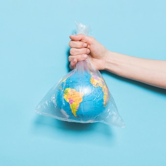 Вид спереди руки, держащей земной шар в полиэтиленовом пакете